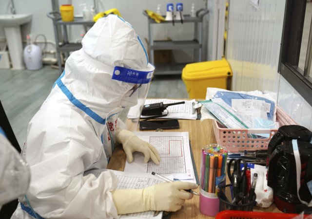 Zaměstnanec nemocnice v čínské Šanghaji je kvůli koronavirovým opatřením oblečen v ochranném obleku.