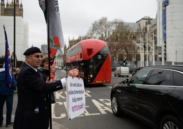 Britský penzista George Cowey mává na vládní auta vjíždějící do areálu parlamentu v Londýně, který 20. března 2019 jednal o otázkách spojených s brexitem. Nápis na ceduli vyzývá k "navrácení britské suverenity".