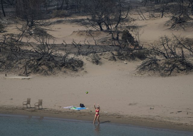 Ani požáry a spáleniště neodradily turisty od hrátek u moře, jako ve čtvrtek 27. července 2023 na pláži poblíž vesnice Gennadi na ostrově Rhodos v jihovýchodním Řecku v Egejském moři.