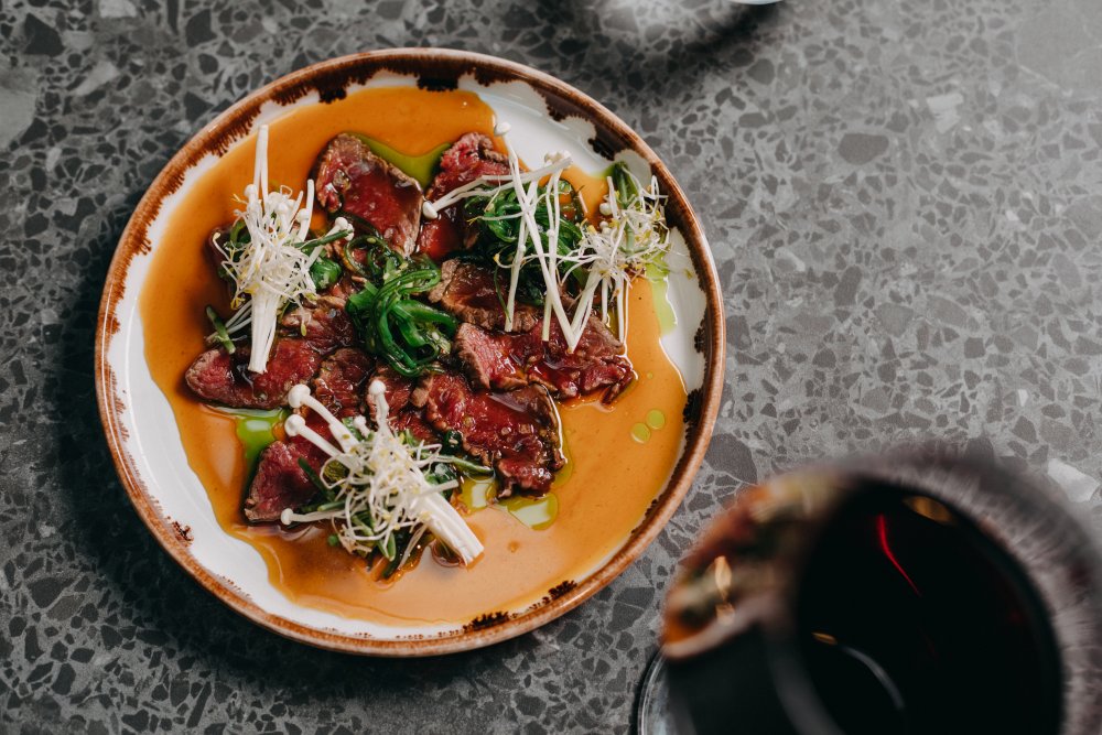 Hovězí tataki je výborně dochucené sezamem a zázvorem, doplňují ho houby enoki a řasy wakame