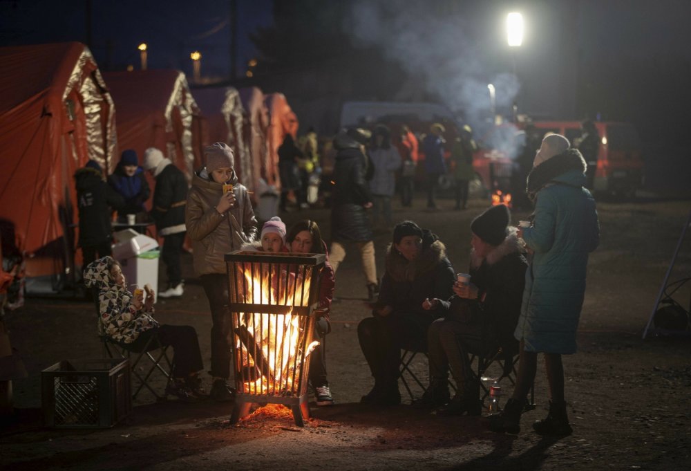 Dospělí a děti se ohřívají u ohně na hraničním přechodě Medyka na polsko-ukrajinských hranicích a čekají na vlak do Krakova. 9. března 2022