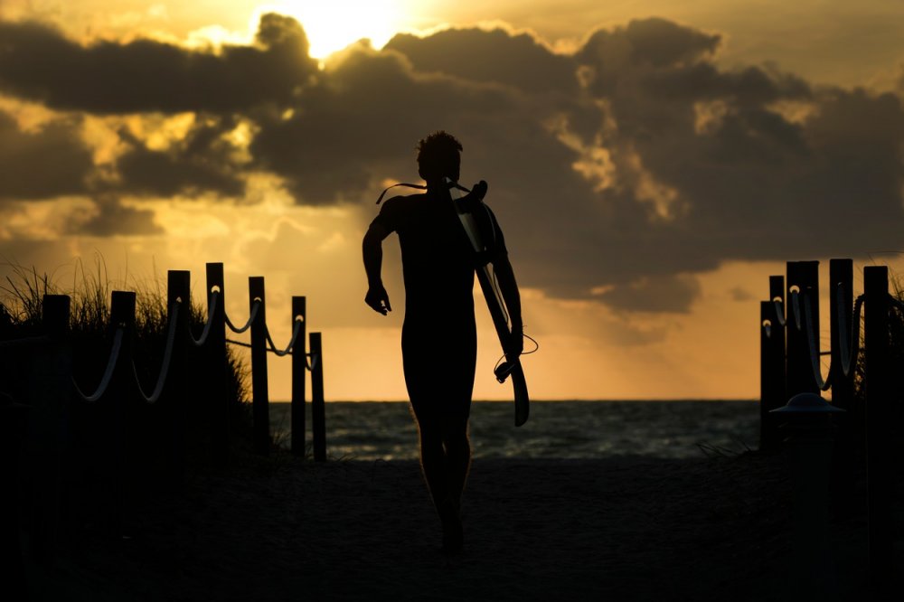 Ranní klid. Surfař míří na pláž, aby stihl vlny, v době východu slunce nad Atlantským oceánem v Surfside na Floridě, čtvrtek 6. dubna 2023. 